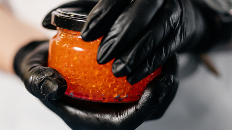 Gloved hands opening a jar of caviar.