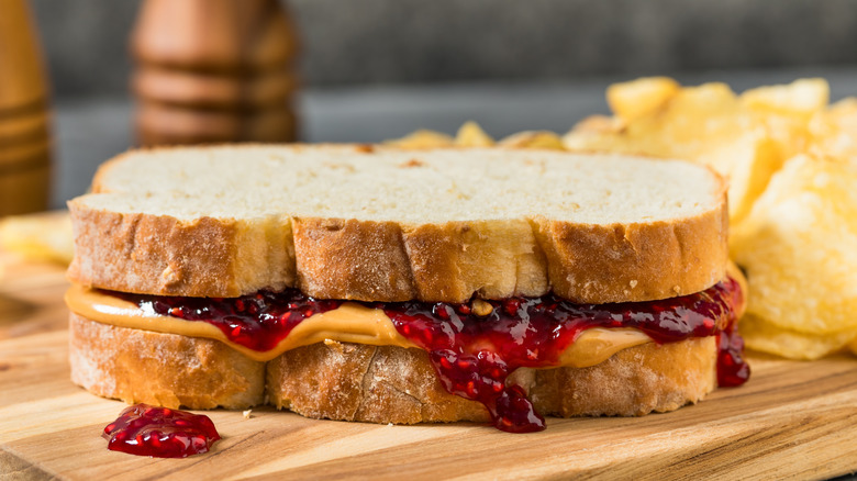 A peanut butter and jelly sandwich with chips on a wooden board