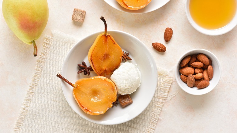 Halved pear in white bowl with star anise and ice cream