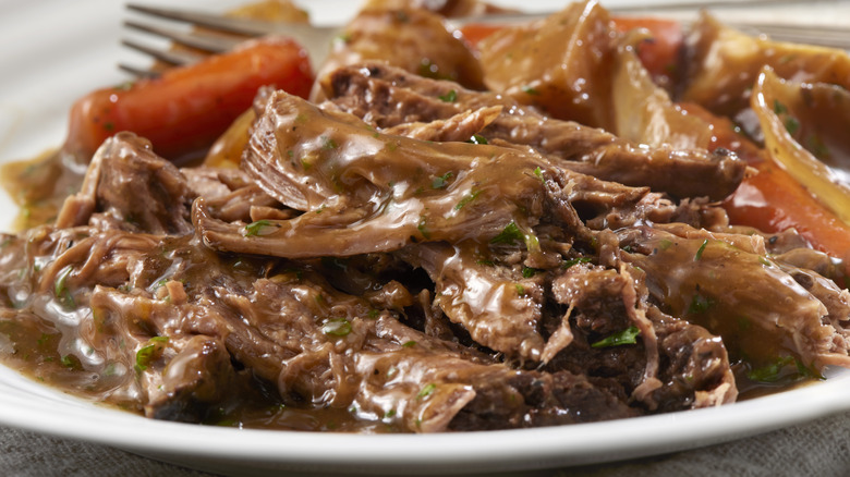A plate of pot roast with onions, carrots, and gravy