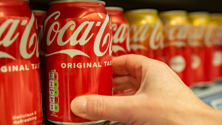 person taking a can of Coca-Cola from a store shelf