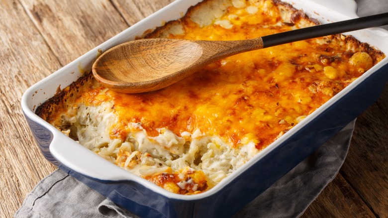 Baked potato casserole with pepperoncini in a casserole dish with a wooden spoon on top.