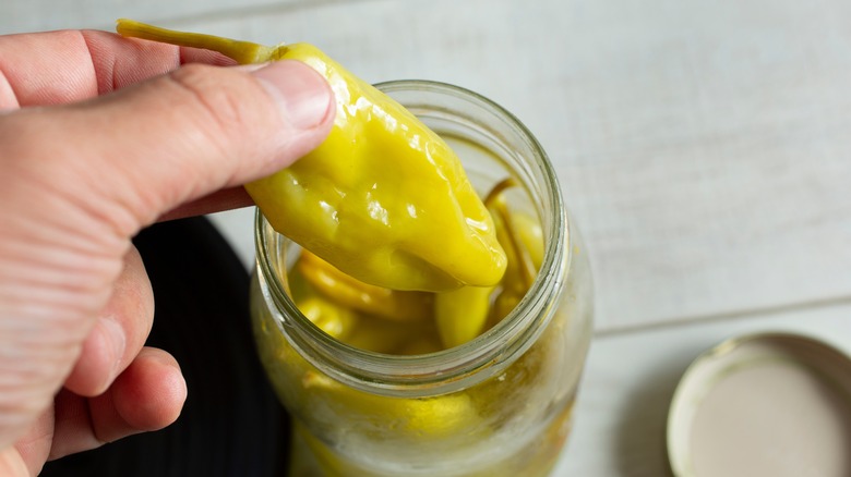 A hand pulls a pepperoncini out of a jar