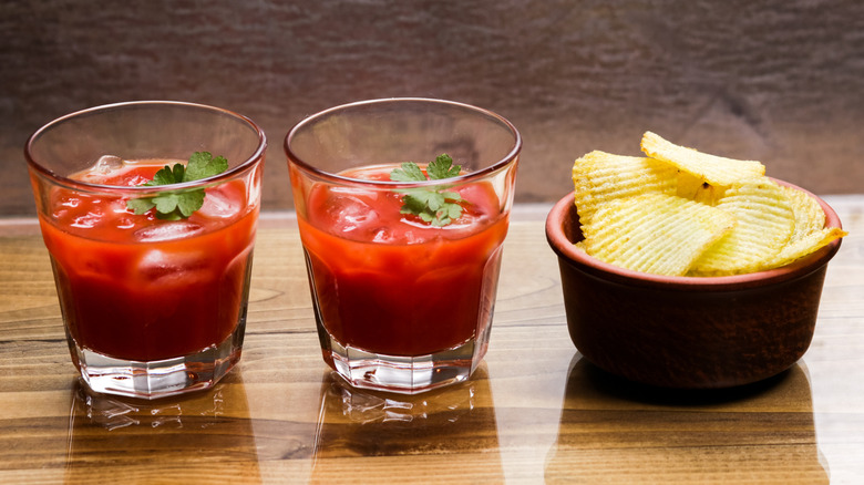 two Bloody Marys with a bowl of potato chips on a shiny wood table