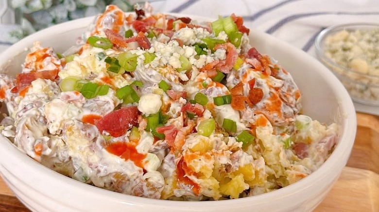 Bowl of creamy Buffalo potato salad topped with bacon, hot sauce, scallions, and blue cheese
