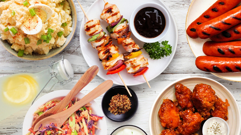 Assorted cookout dishes including potato salad, chicken kabobs, coleslaw, Buffalo wings, and hot dogs