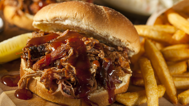 Pulled pork sandwich on wooden board with french fries