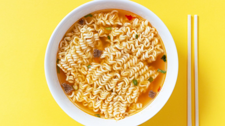 Instant ramen in a white bowl with chopsticks next to it on a yellow background