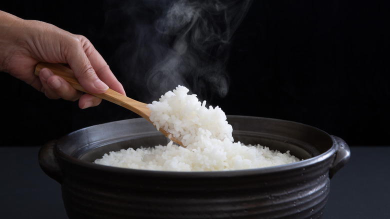 Hands use wooden spoon to scoop hot rice