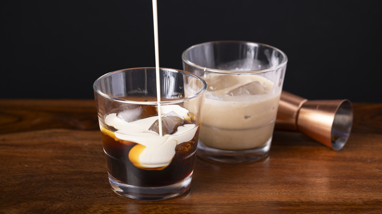 A dark cocktail with ice and a creamy liquid being poured into it