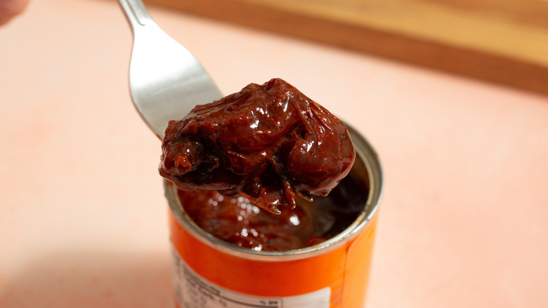 A chipotle in adobo being removed from a can with a fork