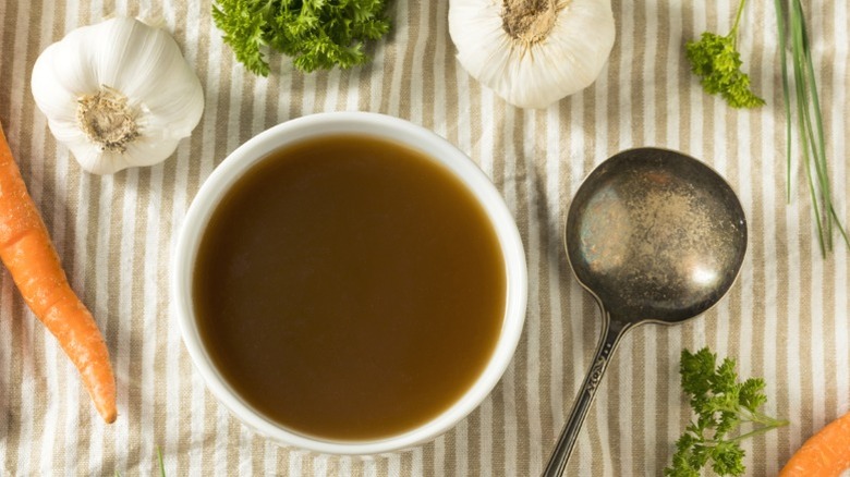 A bowl of beef broth with a spoon and aromatics.
