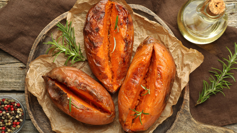 Three baked sweet potatoes split down their center on parchment paper with fresh rosemary sprigs on top