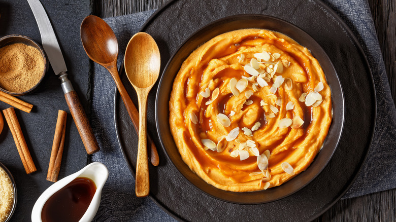 bowl of whipped sweet potatoes with almonds sprinkled on top and wooden serving spoons on the side
