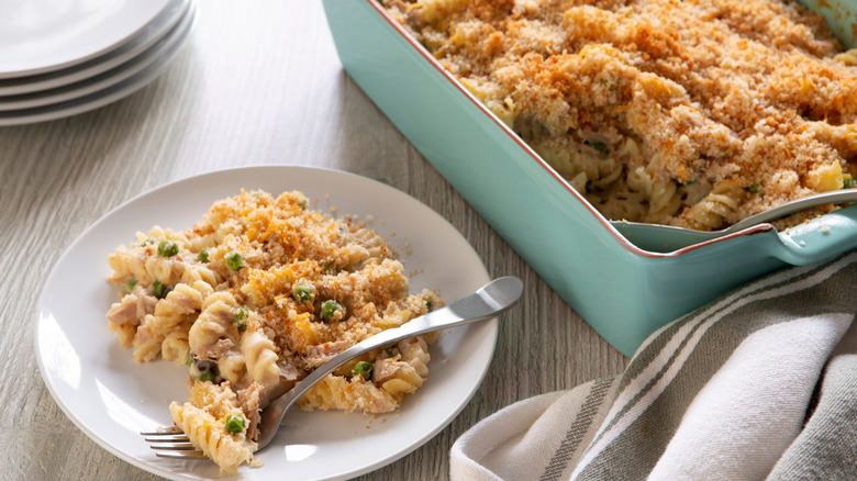Baking dish and plate of tuna casserole with breadcrumbs.
