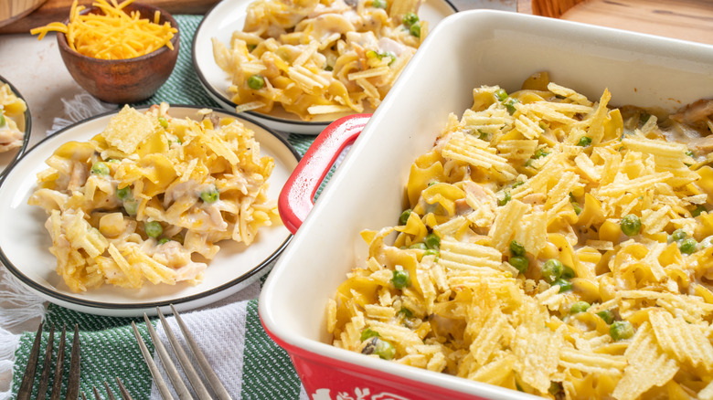 Baking dish and plates of tuna noodle casserole with peas and potato chips.