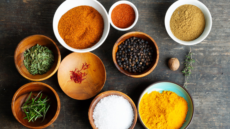 An array of dried spices in bowls against a stone background