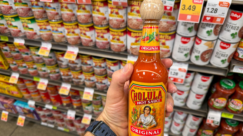 A hand holding a Cholula hot sauce bottle after grabbing it from the store shelf.