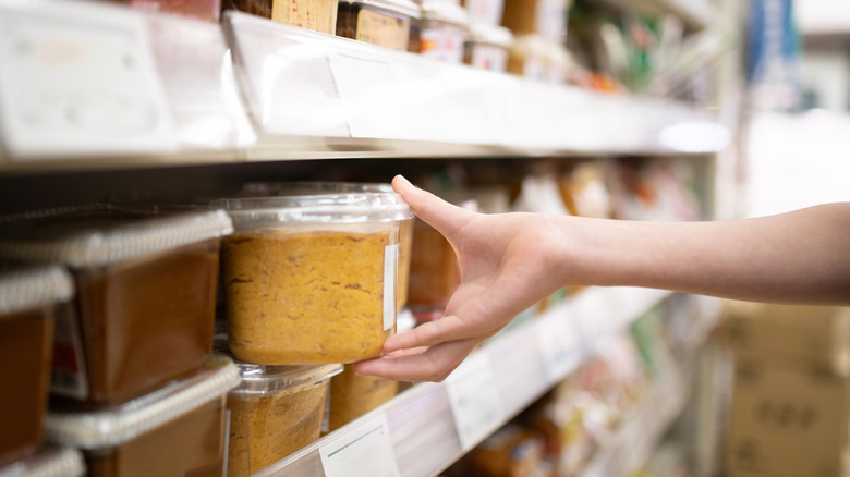 A hand picking white miso paste from a grocery store shelf