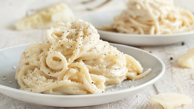 Two shallow white bowls of spaghetti cacio e pepe