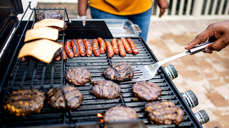 Someone grilling burgers and hot dogs for a cookout