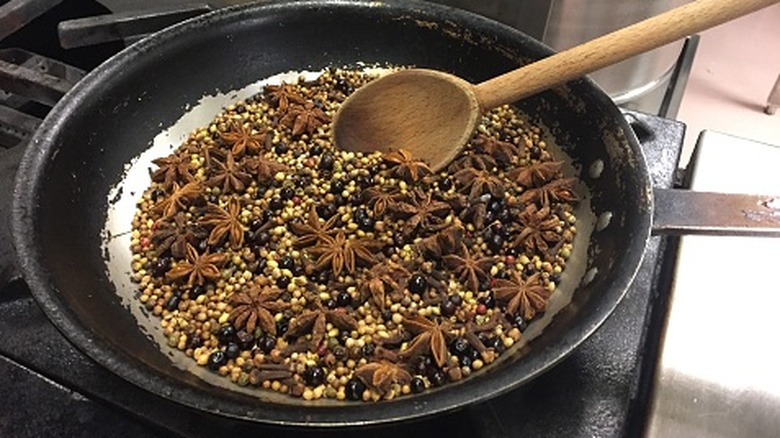 toasting whole spices in a black frying pan with big wooden spoon