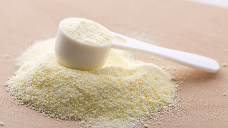 a pile of milk powder on a wooden surface with a powder scooper on it