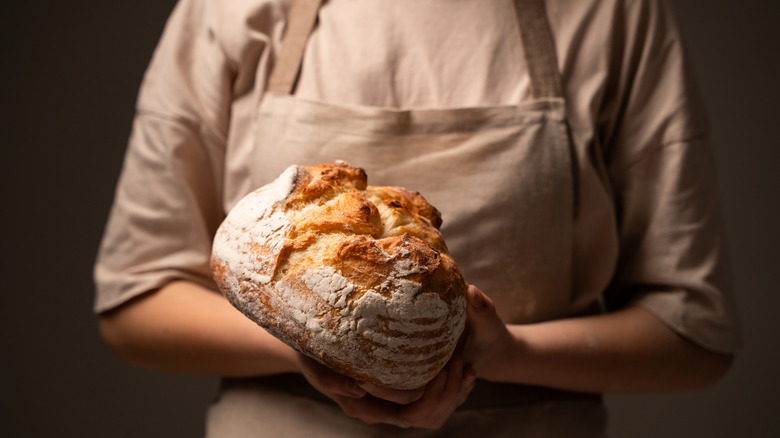 A woman holding a loaf of sourdough bread.