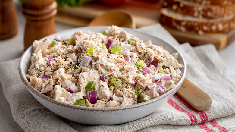 A bowl of tuna salad with celery and onions on a tablecloth.