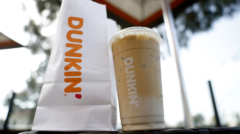 A Dunkin iced coffee next to a Dunkin' paper bag outside