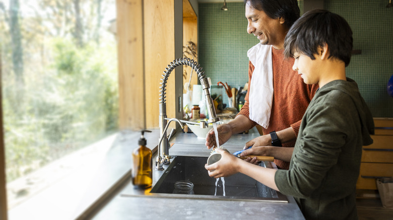 Father and son washing dishes at the kitchen sink in front of big window