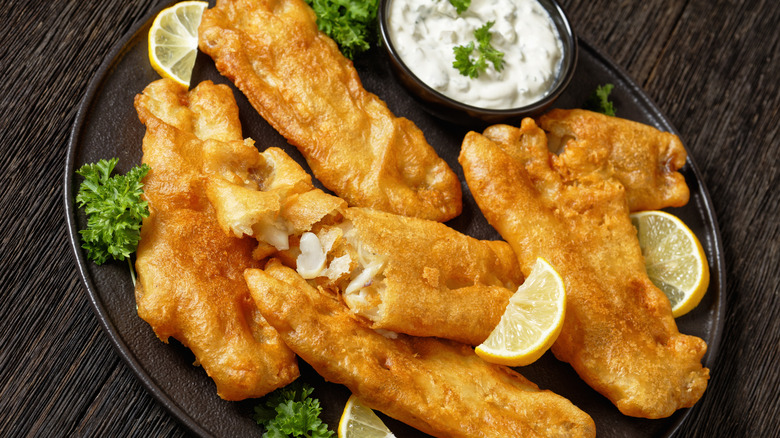 Fried cod on a black plate with lemons and tartar sauce