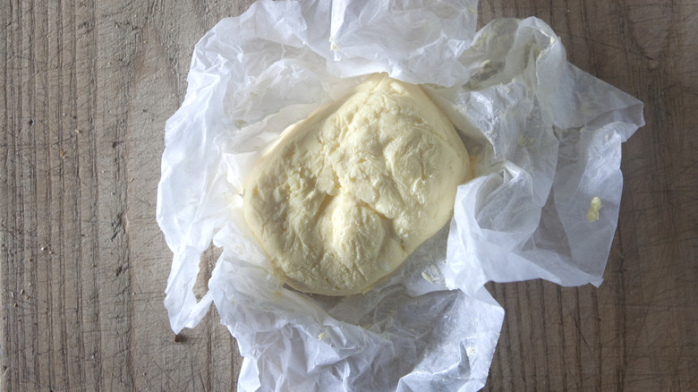 A large roll of Devonshire butter wrapped in waxed paper on a wooden tabletop