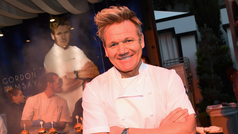 Gordon Ramsay standing in front of trays of burgers in a restaurant