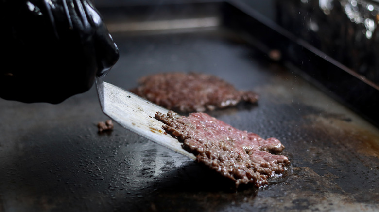 A hand flipping a smash burger with a spatula