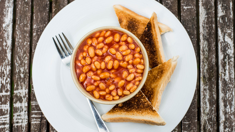 A bowl of baked beans and triangles of toast on a white plate