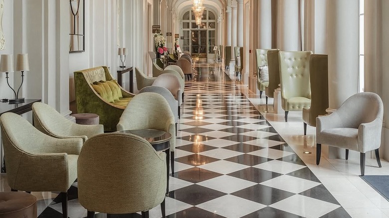 Elegant waiting area outside Gordon Ramsay au Trianon restaurant, with marble floors along long corridor with columns and fancy chairs