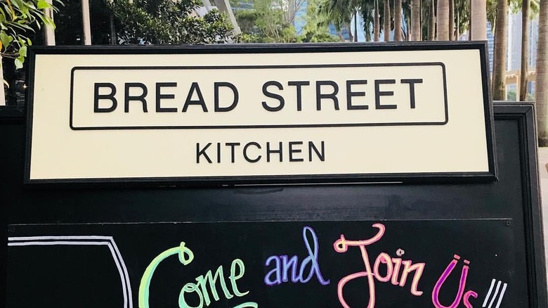 Bread Street Kitchen menu board outside restaurant entrance in front of promenade lined with palm trees