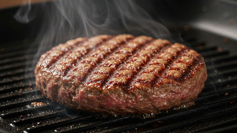 Steaming beef burger patty on grill pan