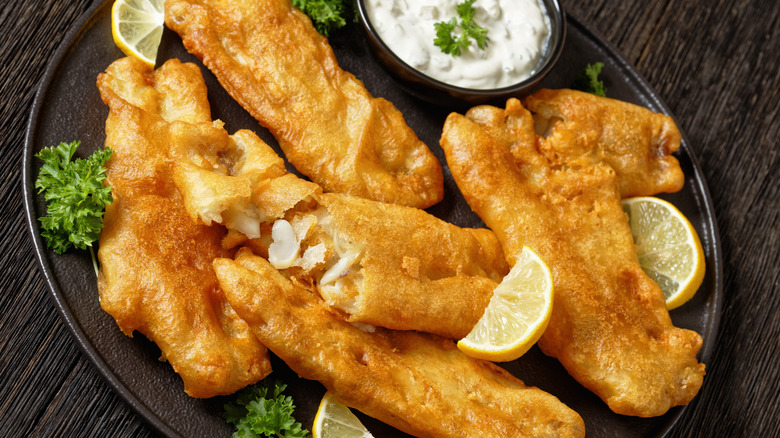 Fried cod on a black plate with lemons and tartar sauce