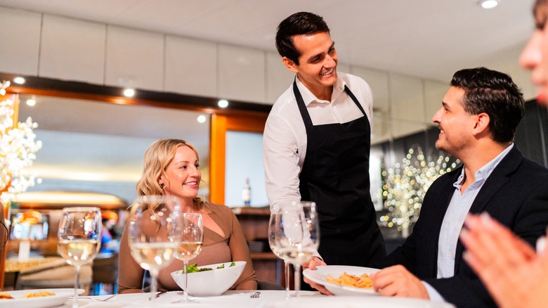 Person smiling while being served dish in a nice restaurant