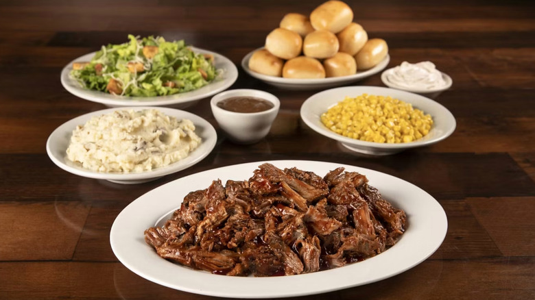 Texas Roadhouse Pulled Pork Family Pack with dishes of corn, mashed potato, salad, and bread rolls
