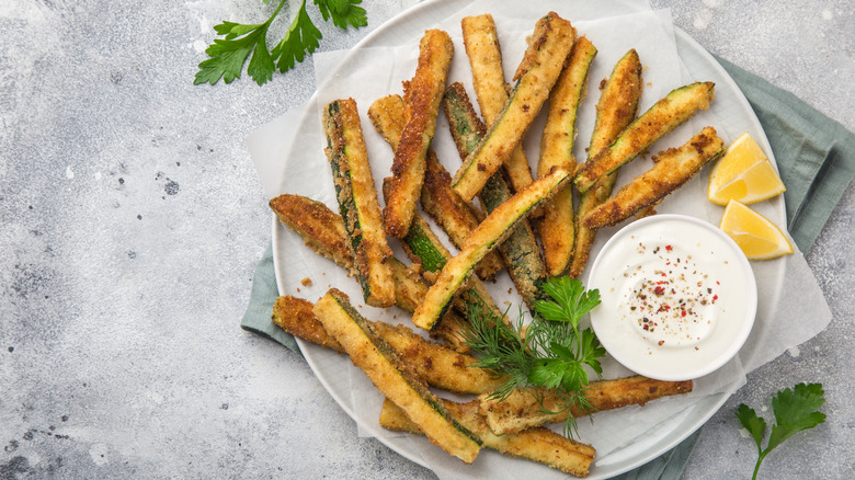 zucchini fries on a white plate with a yogurt dip, herbs, and lemon