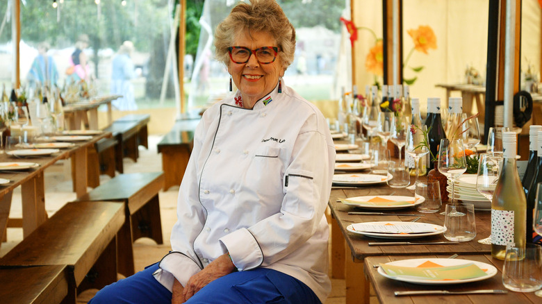 Prue Leith smiling in her chef's coat and blue pants at a dining event.