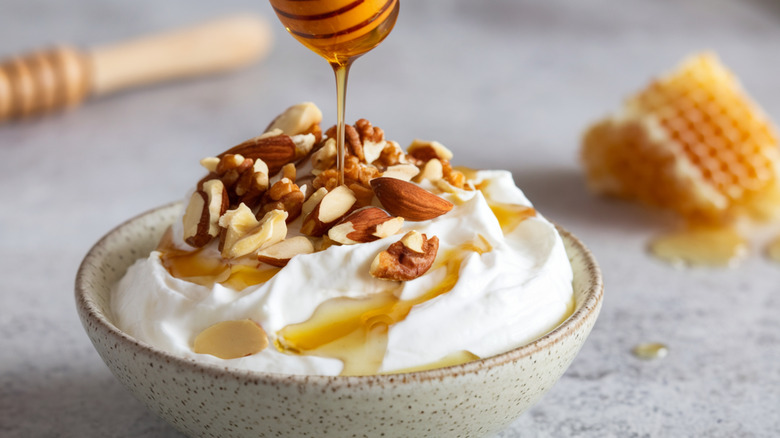 Drizzling honey on bowl of thick yogurt with nuts