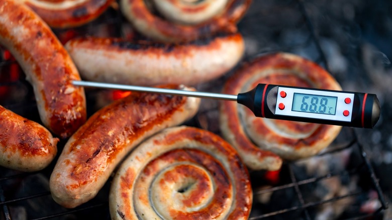 Meat thermometer stuck into grilled sausage on the grill
