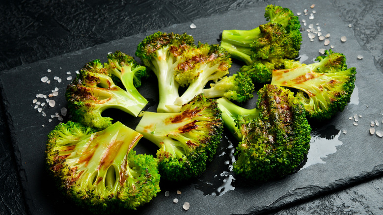 Grilled broccoli with balsamic sauce on a black slate plate.