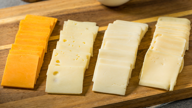 Four different types of cheeses cut into squares on a wooden cutting board