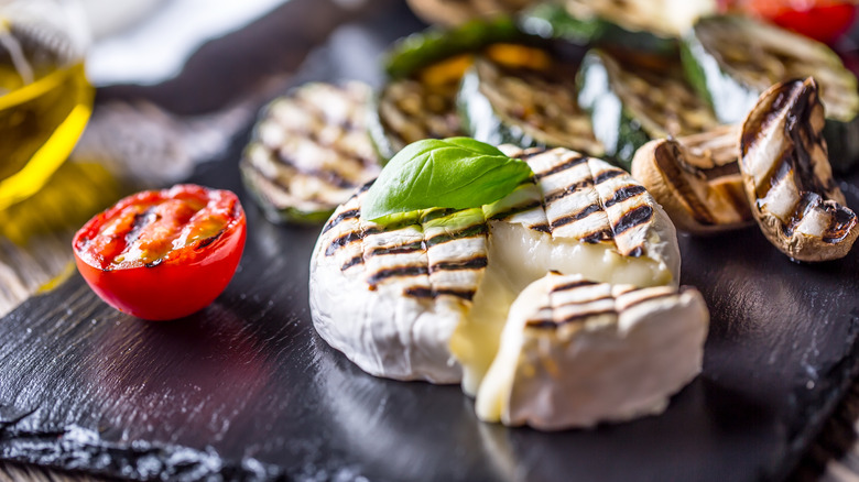 Grilled whole Camembert cheese on a platter with grilled vegetables
