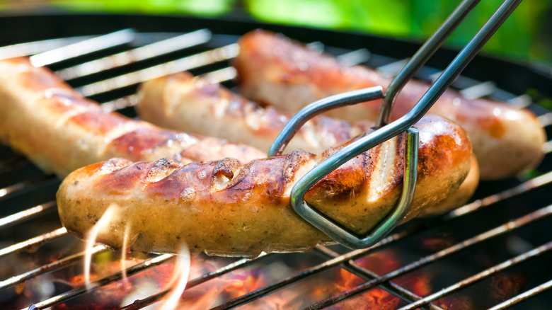 Several hot dogs on a grill, with one being turned